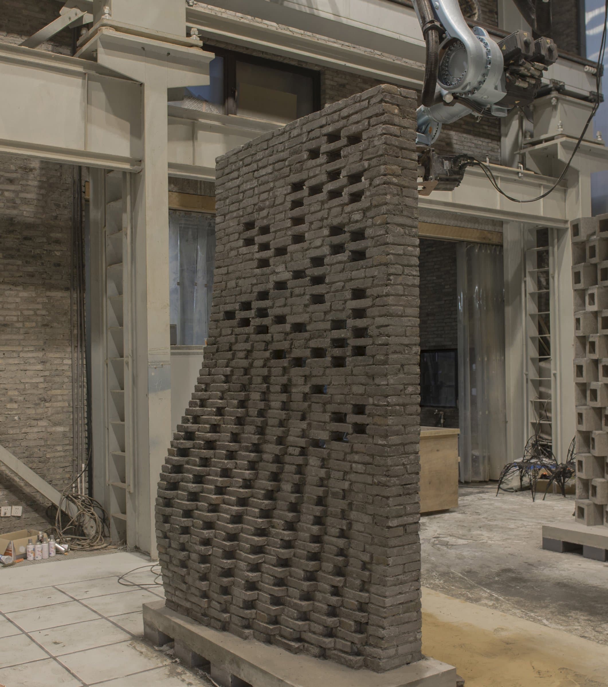 Robotic arm laying recycled grey bricks on the curved Chi She wall replica