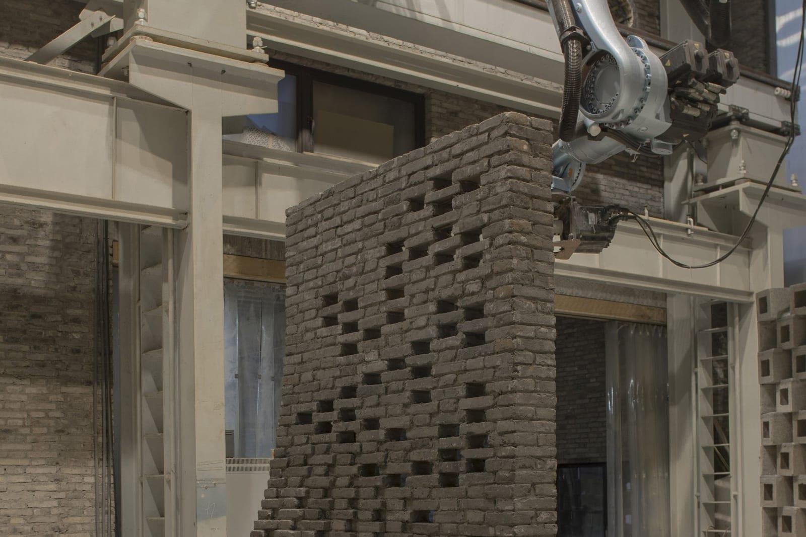Robotic arm laying recycled grey bricks on the curved Chi She wall replica