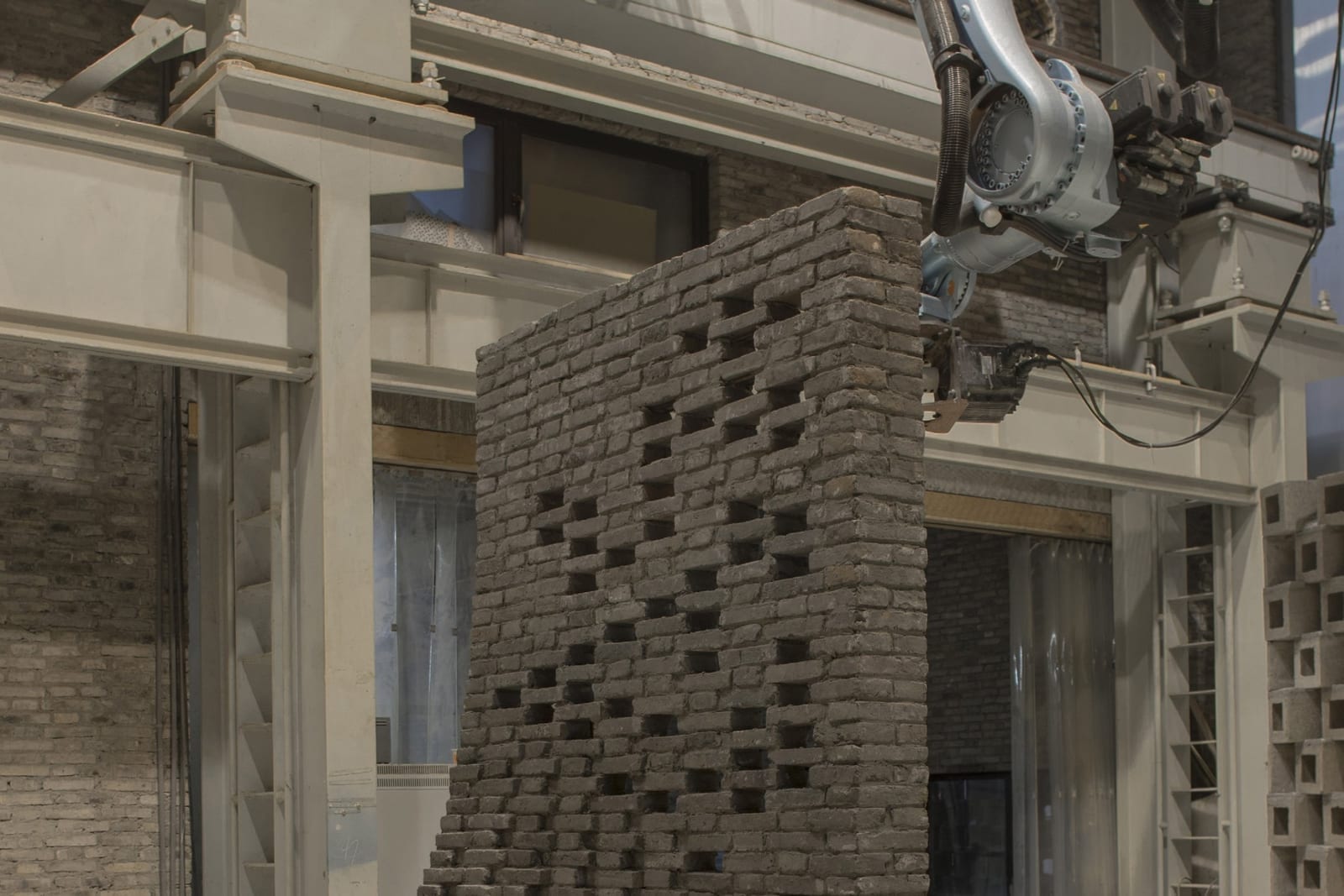 Robotic arm laying recycled grey bricks on the curved Chi She wall replica