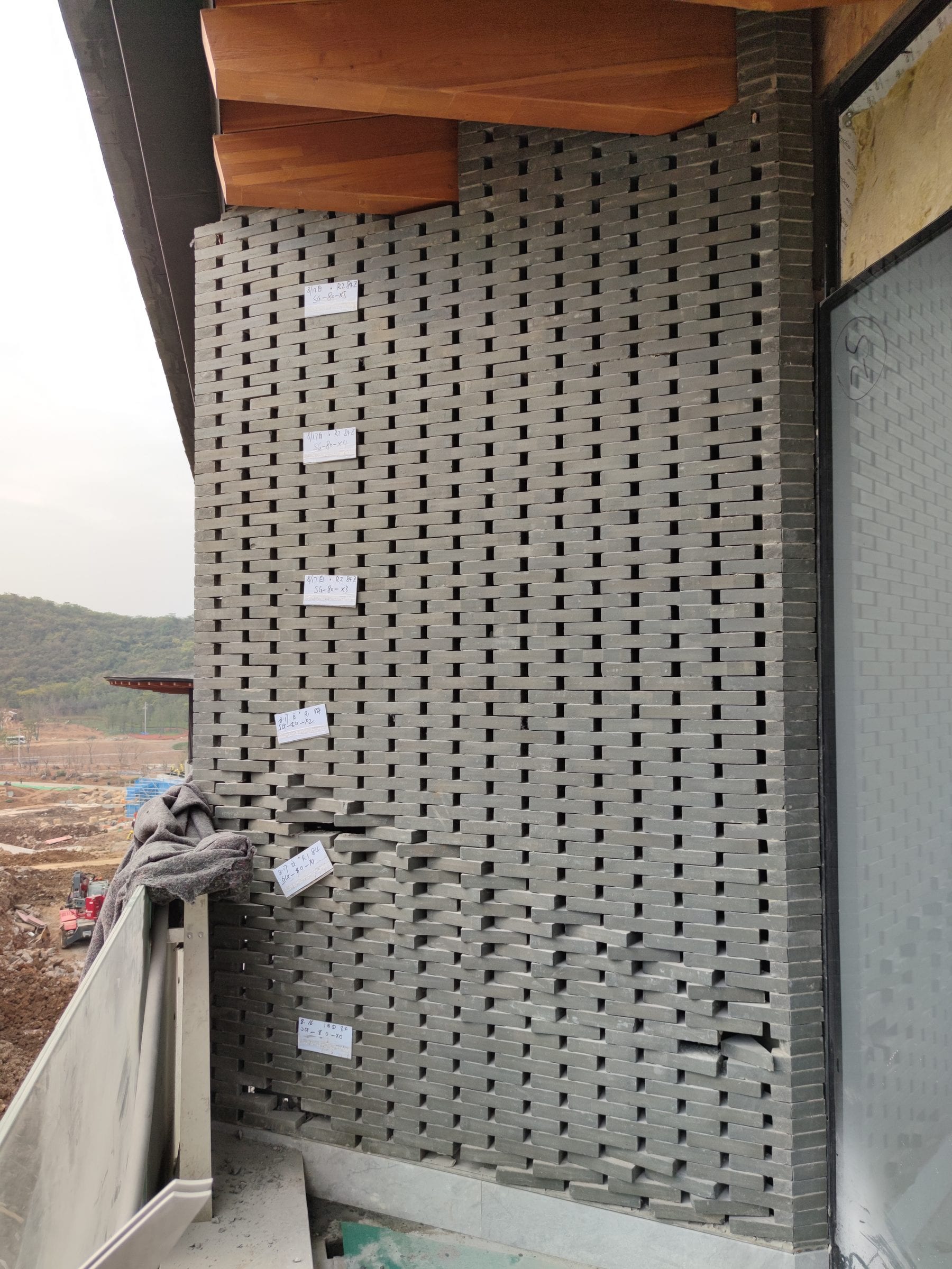 Curved perforated brick facade under the timber soffit during on-site coordination