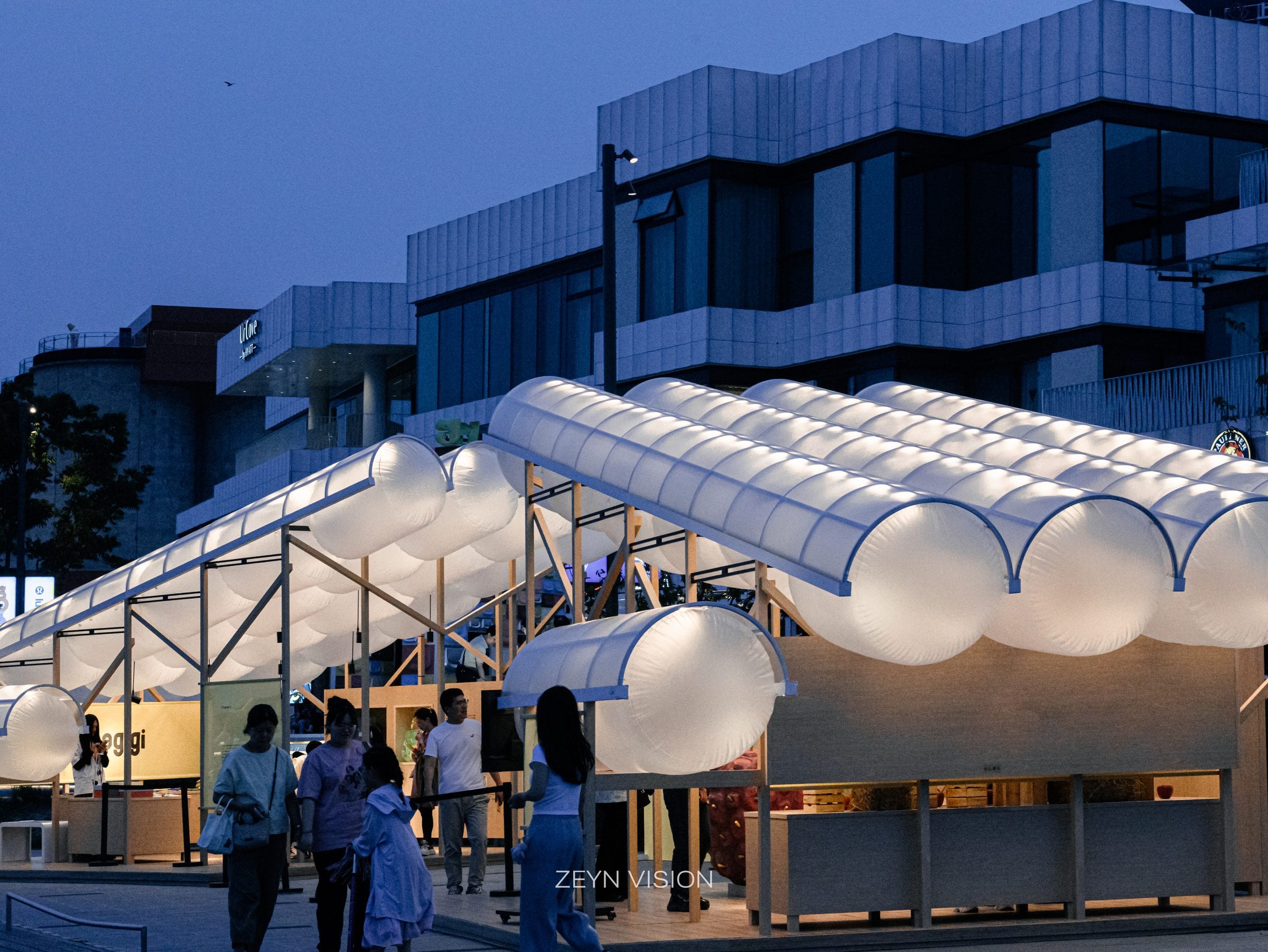 The two hunogigi pavilions glowing at dusk with visitors gathering on the promenade