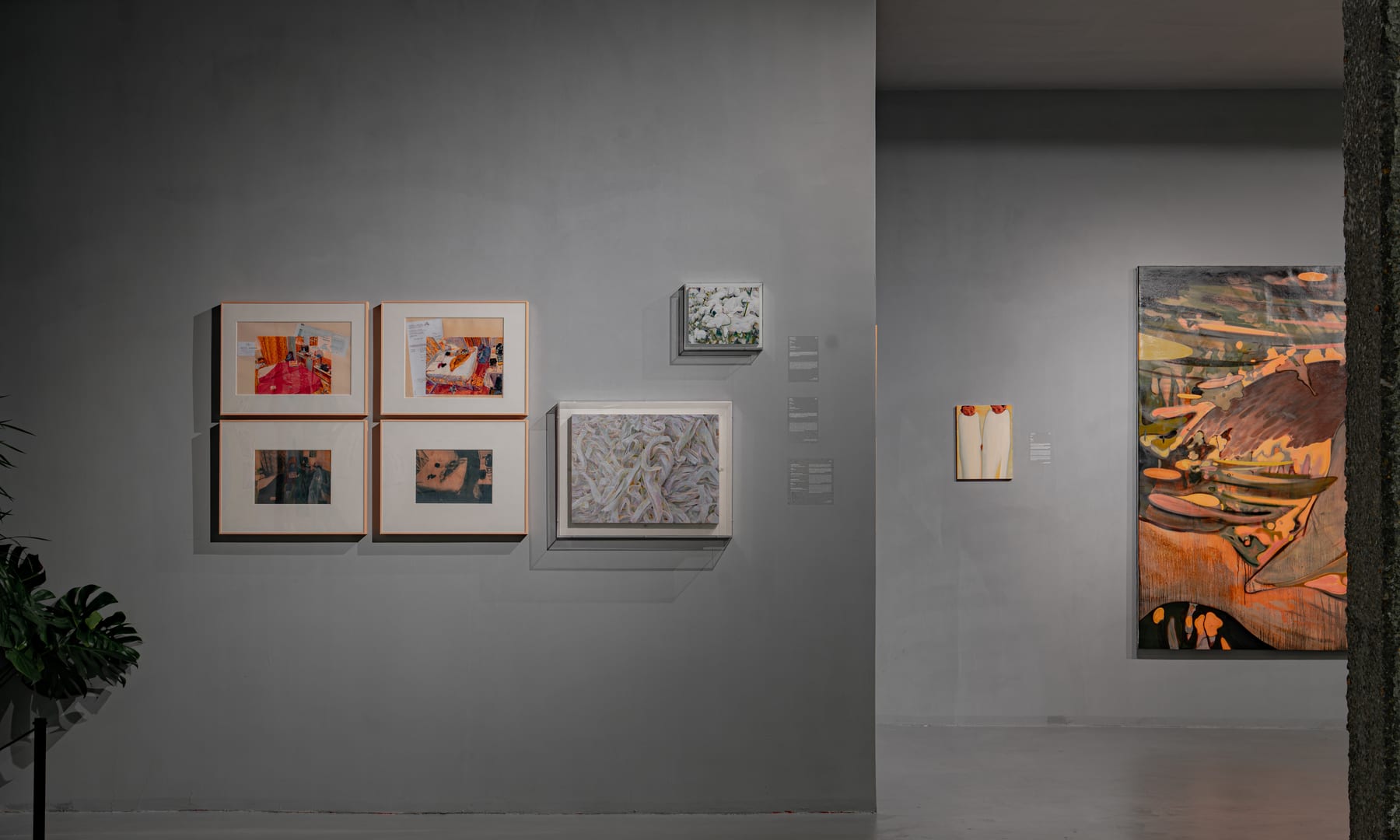 Warm-lit gallery wall of framed works beside a tree-trunk column