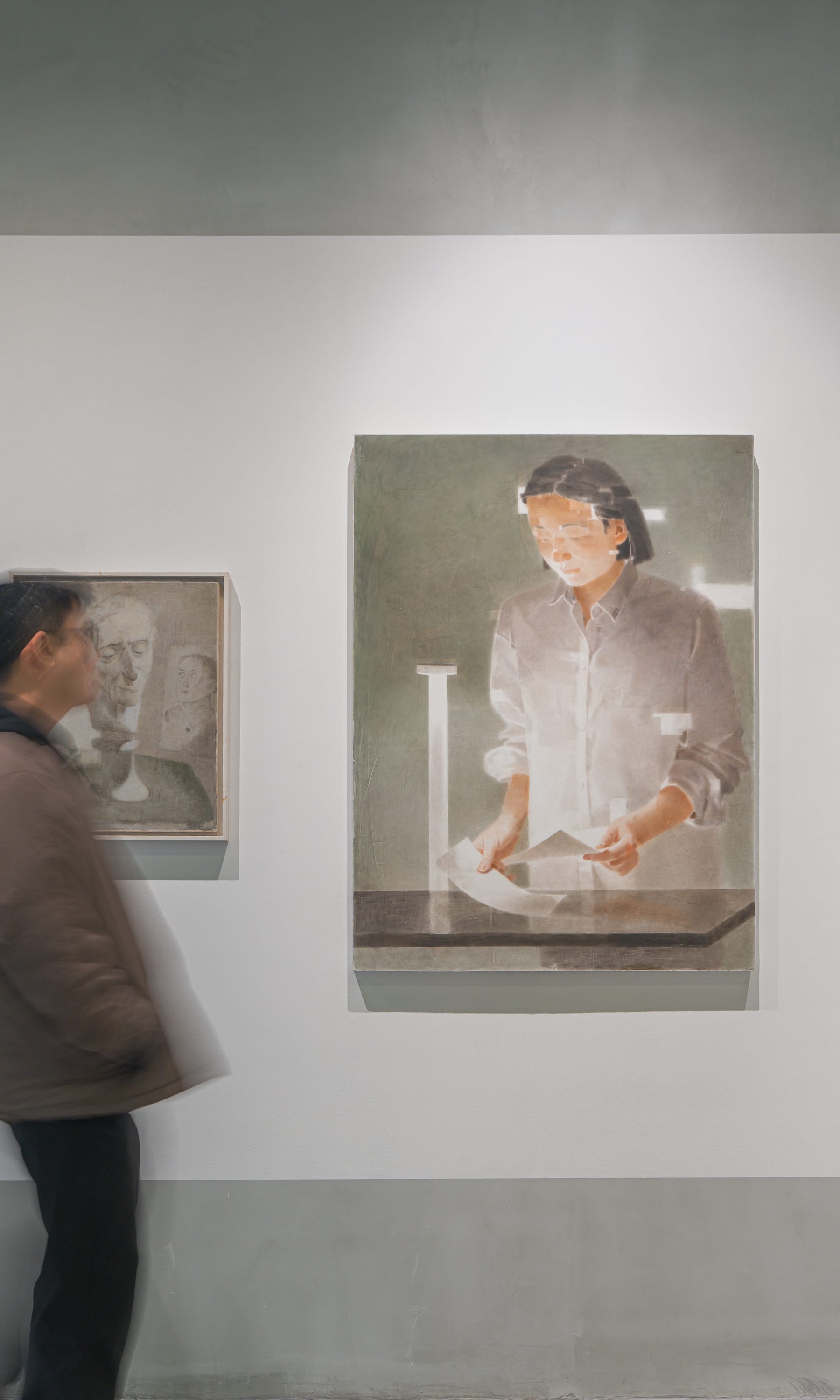 A visitor pausing before portraits, beside a painting of a woman reading