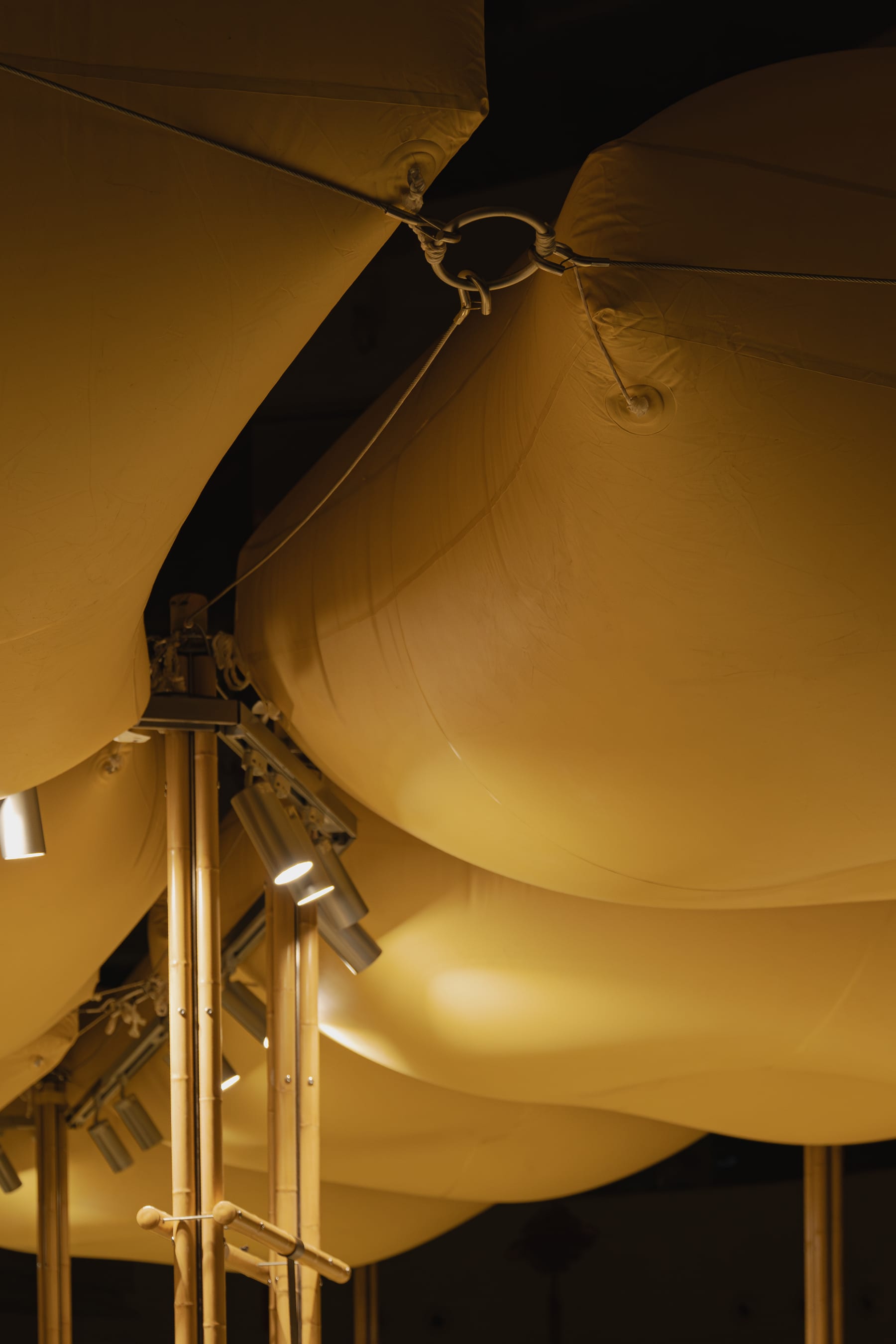 Ring node clamping four inflatable pillows to a bamboo-steel column, spotlights below