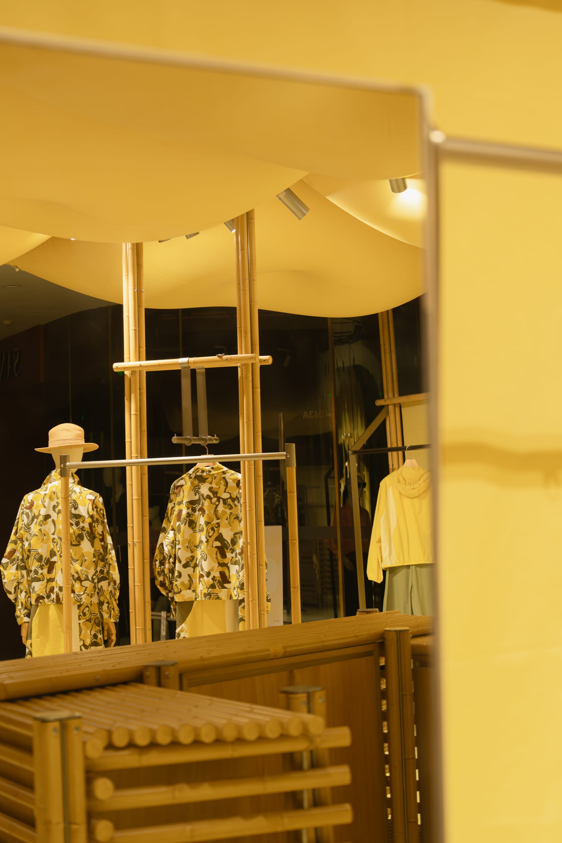 Two mannequins framed between bamboo columns, membrane edge in the foreground