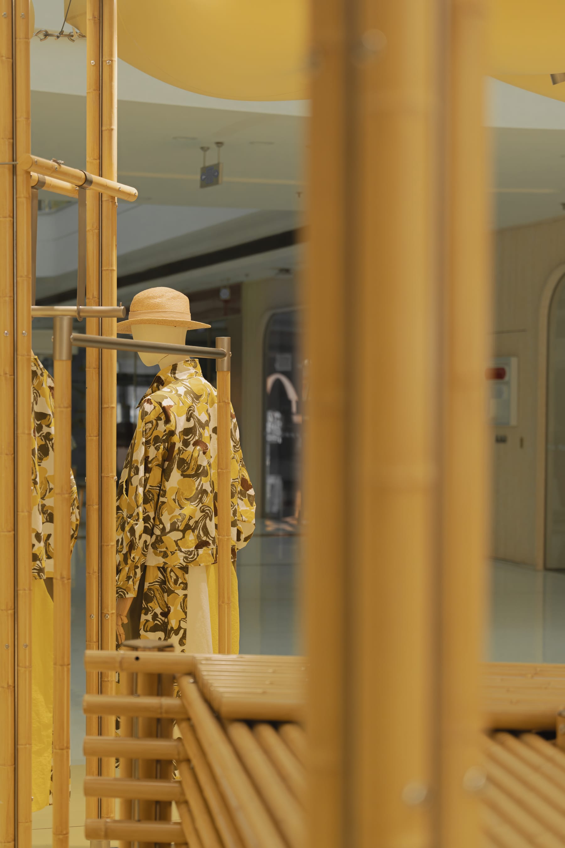 Mannequin in floral suit and straw hat framed by a bamboo column, daylight
