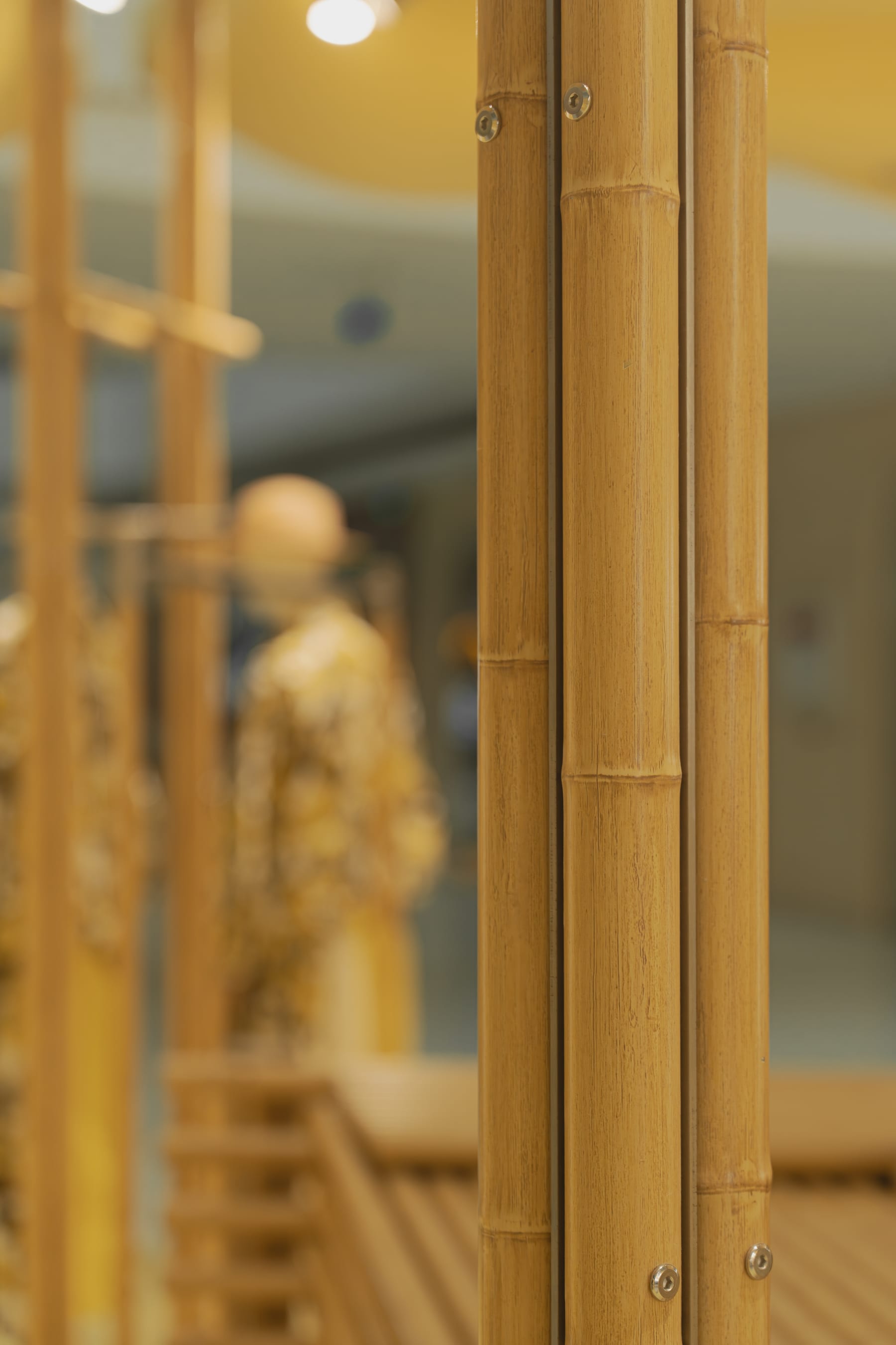 Bolted bamboo column detail, mannequin dissolving into bokeh