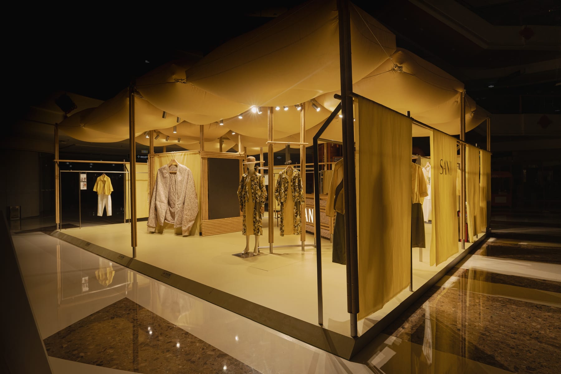 Three-quarter view of the pavilion at night, canopy and membranes reflected in the polished floor