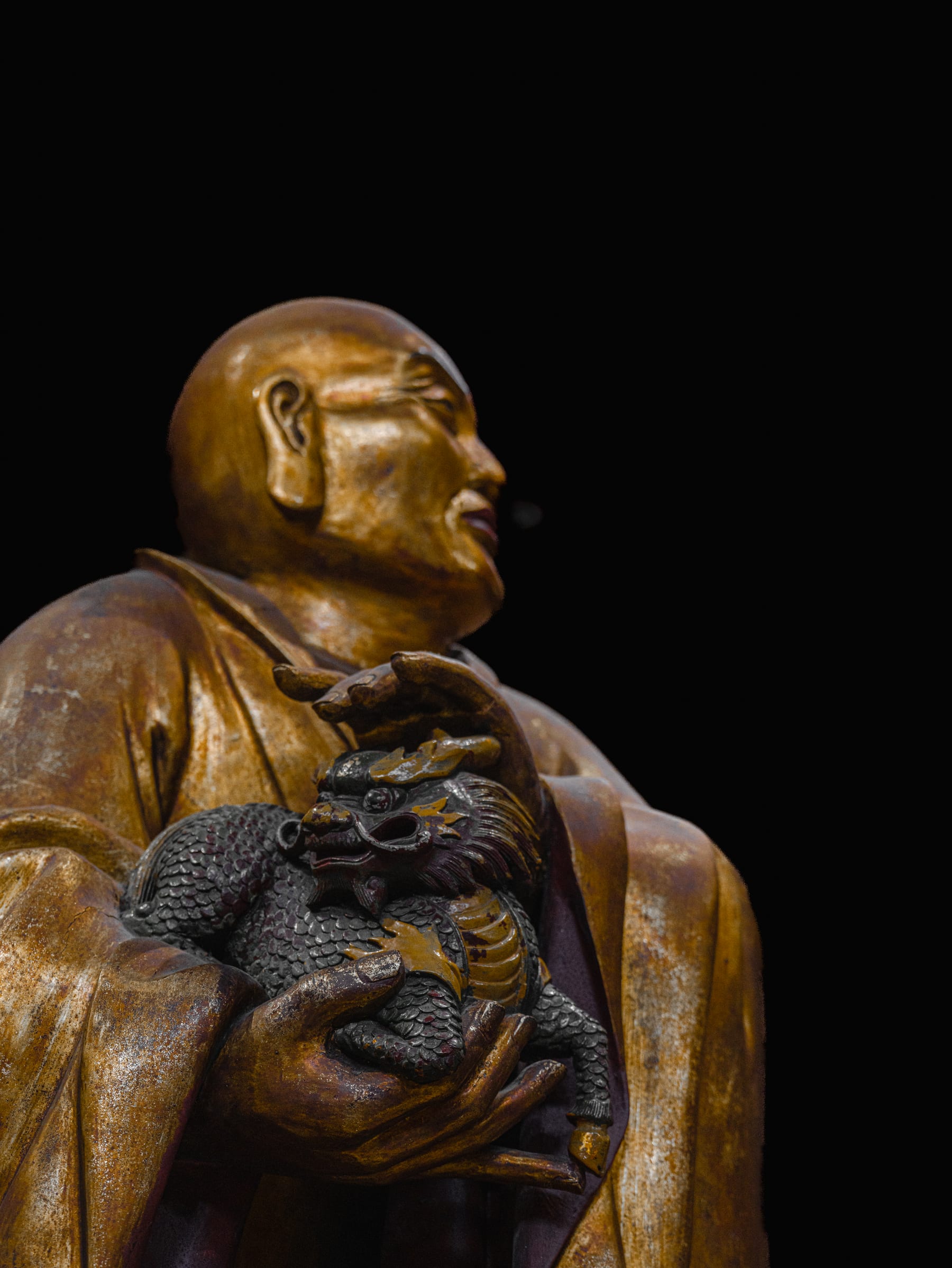 Profile of a golden luohan against the dark hall